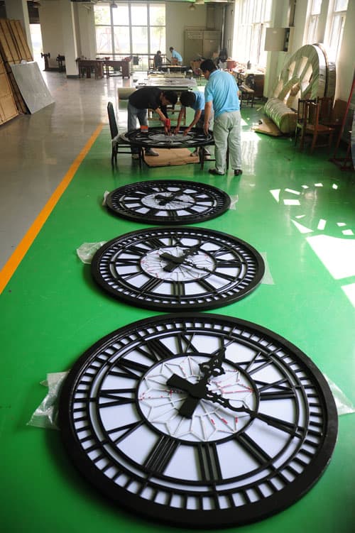 Large clock faces being assembled and checked on the factory floor.