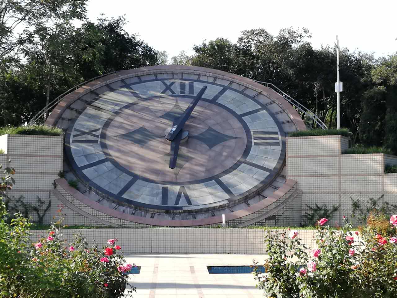 Large stone-faced floral clock framed by roses and greenery.