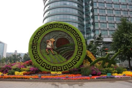 Vertical floral clock installation framed by colorful flower beds.