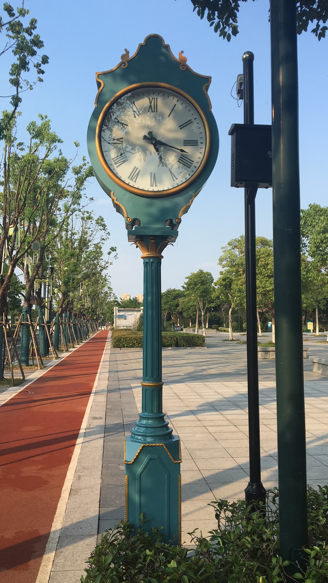 Green street clock installed beside a landscaped cycle path.