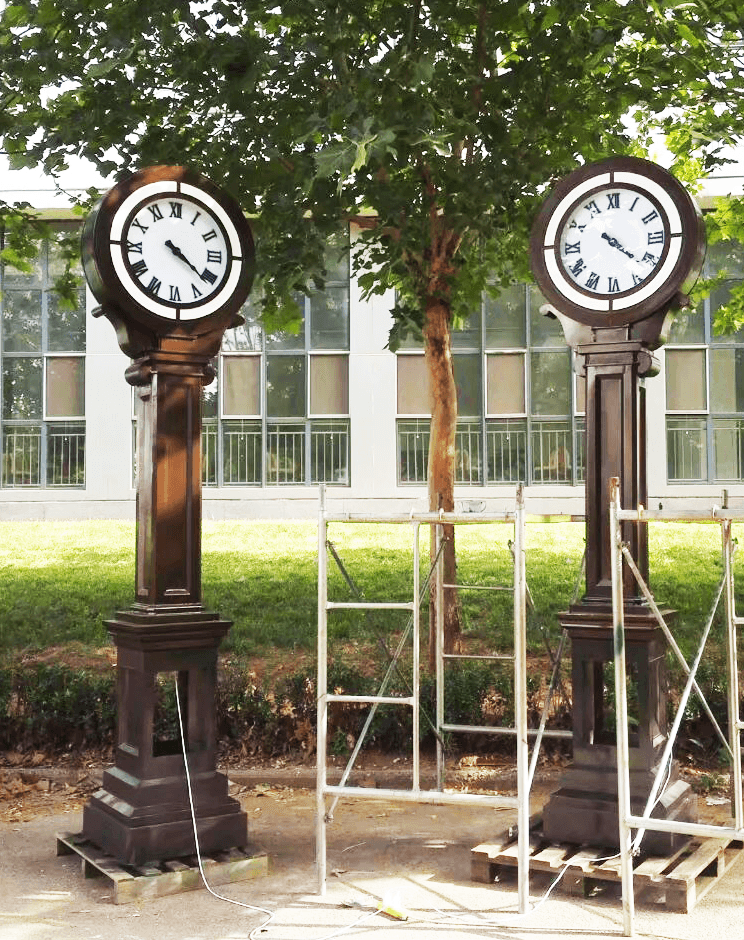 Two matching double-sided landscape clocks installed on a landscaped campus.