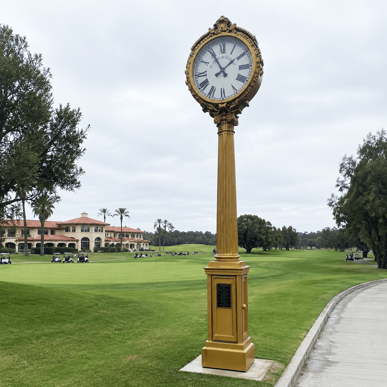 Ornate gold street clock set beside a landscaped golf course.